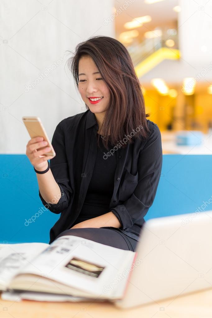 Asian college student sitting with a laptop, a book and a phone
