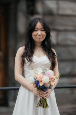 Tarihi şehirde parlak buketli beyaz gelinlik içinde güzel bir Asyalı gelin. Yüksek kalite fotoğraf