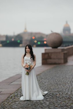 Tarihi şehirde parlak buketli beyaz gelinlik içinde güzel bir Asyalı gelin. Yüksek kalite fotoğraf