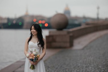 Tarihi şehirde parlak buketli beyaz gelinlik içinde güzel bir Asyalı gelin. Yüksek kalite fotoğraf