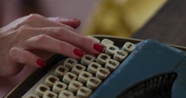  Kadın eski mavi bir daktiloyla yazı yazıyor. Mektuplar anahtarlara kazınmış. Çerçevesinde kırmızı tırnak askılı bir kızın elleri var. Bir kitap yazıyor. İçeride. Yüksek kalite 4k görüntü