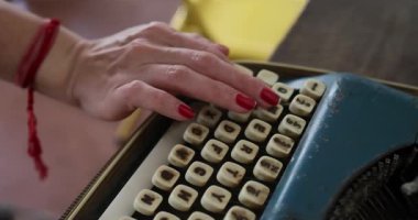  Kadın eski mavi bir daktiloyla yazı yazıyor. Mektuplar anahtarlara kazınmış. Çerçevesinde kırmızı tırnak askılı bir kızın elleri var. Bir kitap yazıyor. İçeride. Yüksek kalite 4k görüntü