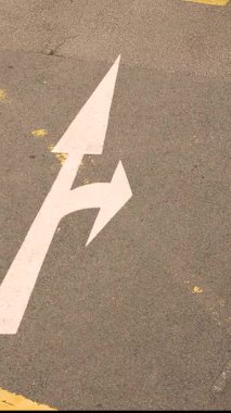 Asfalttaki beyaz yol okunun işaretleri izin verilen yönü gösterir: düz veya sola dönüş, trafik rehberliğini, sokak altyapısını, kentsel yol kavramını, güvenli sürüş ve şehir ulaşımını göstermektedir. Yüksek kalite 4k görüntü