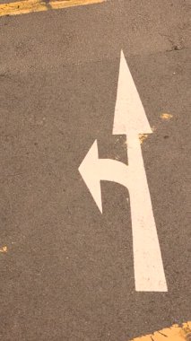 Asfalttaki beyaz yol ok işaretleri izin verilen yönü gösterir: düz veya sağa dönüş, trafik rehberliğini, sokak altyapısını, kentsel yol kavramını, güvenli sürüş ve şehir ulaşım sahnesini göstermektedir. Yüksek kalite 4k görüntü