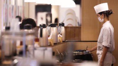 Şık Asyalı kadın şef, beyaz şapka takıyor ve şef önlüğü giyiyor. Restoran mutfağında yemek hazırlıyor, profesyonel mutfak işlerini, şef yaşam tarzını, modern aşçılığı ve gurme yemek hazırlıklarını gösteriyor. Yüksek kalite 4k görüntü