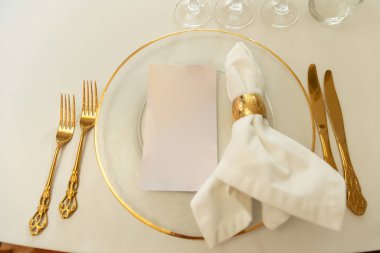 Lezzetli bir ziyafet için beyaz bir masada temiz bir tabak, peçete ve çatal bıçak hazır. Neşeli, unutulmaz bir şenlik için mükemmel bir zemin. Pahalı gümüşten yapılmış düğün galası öğle yemeği aletleri. Yüksek kalite fotoğraf