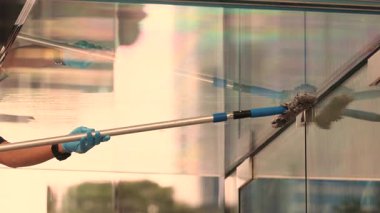 Alışveriş merkezi girişinin üstündeki şeffaf cam örtüyü paspas hareketiyle temizliyorum.