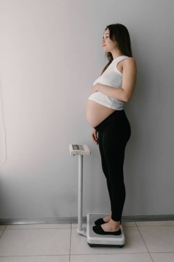 Hamile esmer kadın hamilelik süresince tartıların üzerinde duruyor. Yüksek kalite fotoğraf