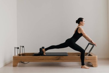 Pilates yenilikçi eğitim makinesi. Atletik kadın, profesyonel yenilikçi makinede pilates yapıyor. Siyah bir vücut giysisi giyiyor. Eğitim, güç odaklı özel pilates ekipmanı kullanır