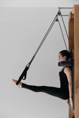 Modern bir stüdyoda siyah mayo giyen beyaz Avrupalı bir kadın olarak kullanılan pilates reformist eğitim makinesi, fitness yaşam tarzı dengesini gösteren beyaz bir duvara karşı kontrollü pilates egzersizleri yapıyor. Yüksek kalite fotoğraf