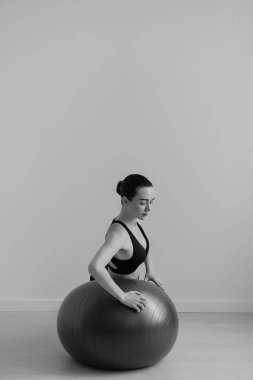 Stüdyoda kadın pilates topuyla antrenman yaparken çekilmiş siyah beyaz bir fotoğraf.