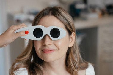 Tıbbi pratisyen kadın hastaların gözlerinin yakınına bir polarizasyon kalkanı yerleştirir. Yapılandırılmış görsel değerlendirme sırasında, görsel teçhizatın tam olarak nasıl kullanıldığını gösterir. Yüksek kalite fotoğraf