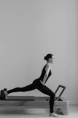 Zayıf bir kadın, siyah beyaz fotoğraf ile Pilates Reform Makinesi üzerinde alıştırma yapıyor.