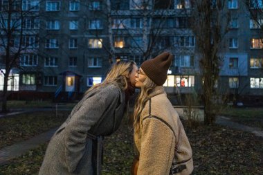 İki kadın, kışın akşam yerleşim bölgesinde yanaktan öpücükle selamlaşır.