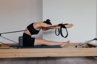 Pilates reformatörü üzerinde eğik katlama egzersizleri yapan kız