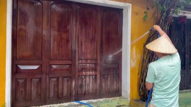 Vietnamlı şapkalı bir adam ahşap bir kapıyı suyla yıkıyor. Yüksek kalite 4k görüntü