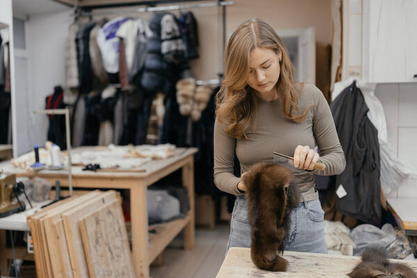 Beautiful female furrier crafting mink fur coats in traditional workshop studio