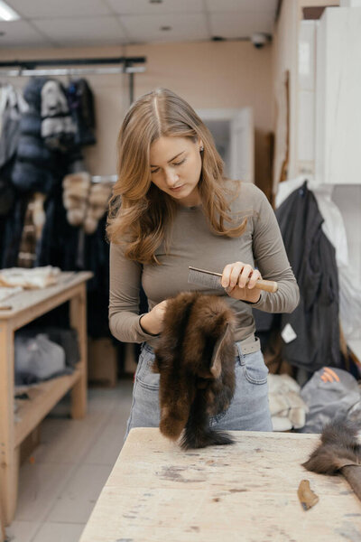 Beautiful female furrier crafting mink fur coats in traditional workshop studio