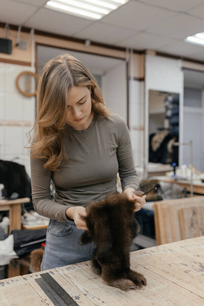 Beautiful female furrier crafting mink fur coats in traditional workshop studio