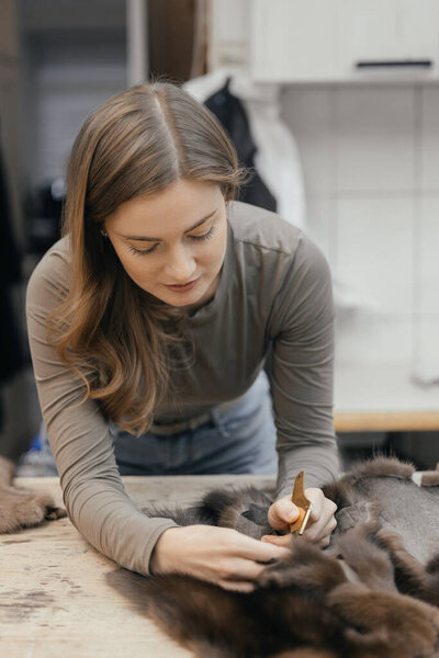 Beautiful female furrier crafting mink fur coats in traditional workshop studio