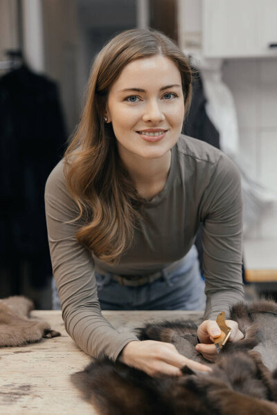 Beautiful female furrier crafting mink fur coats in traditional workshop studio