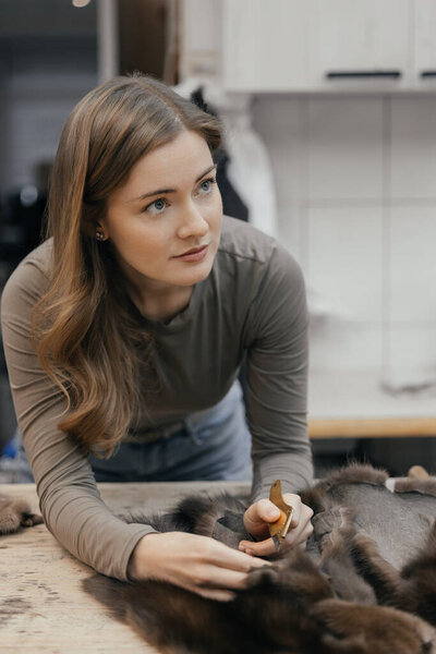 Beautiful female furrier crafting mink fur coats in traditional workshop studio