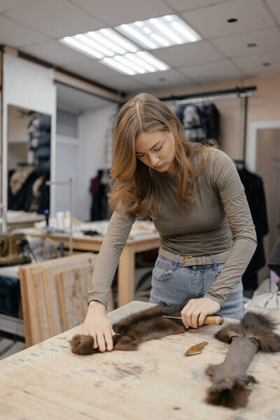 Beautiful female furrier crafting mink fur coats in traditional workshop studio