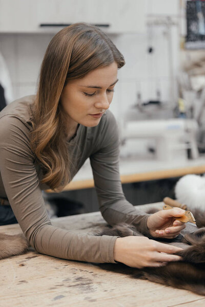 Beautiful female furrier crafting mink fur coats in traditional workshop studio