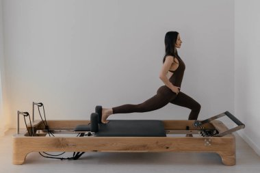 İnce esmerin kullandığı parlak stüdyoya ahşap yerleştirilmiş pilates reformcusu.