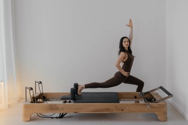 İnce esmerin kullandığı parlak stüdyoya ahşap yerleştirilmiş pilates reformcusu.