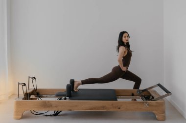 İnce esmerin kullandığı parlak stüdyoya ahşap yerleştirilmiş pilates reformcusu.