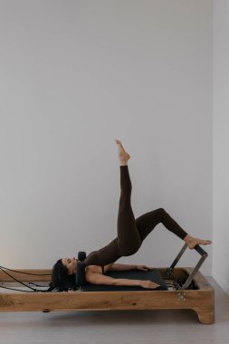 İnce esmerin kullandığı parlak stüdyoya ahşap yerleştirilmiş pilates reformcusu.