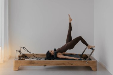 İnce esmerin kullandığı parlak stüdyoya ahşap yerleştirilmiş pilates reformcusu.