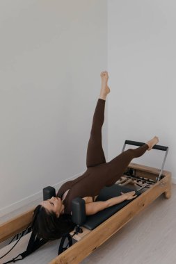 İnce esmerin kullandığı parlak stüdyoya ahşap yerleştirilmiş pilates reformcusu.