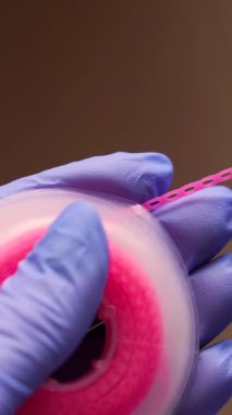 Diş aleti kullanılarak bobinden çıkarılan mor ortodontikli elastik bağın yakın plan görüntüsü. Eldivenli doktor elleri klinik ortamdaki ortodontik prosedürü tam olarak gerçekleştiriyor.