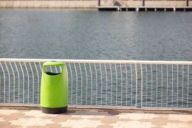 Şehir nehir kenarı boyunca kentsel temizlik, kamu temizliği, peyzaj tasarımı, çevre bakımı ve düzenli şehir yaşamını destekleyen organize liman alanlarını vurgulayan canlı yeşil çöp konteynırlarına yakından bakın.