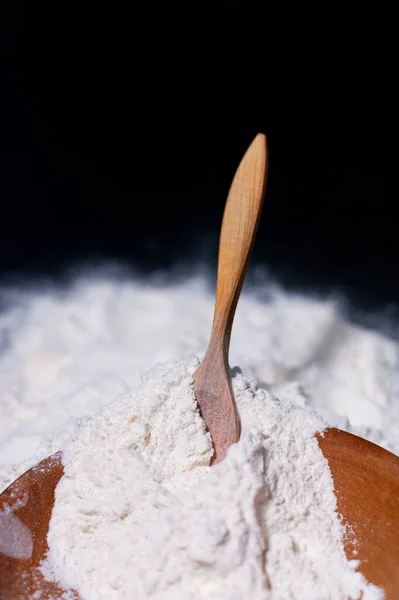 Farina di grano bianco in una tazza e sulla superficie del tavolo. Cucchiaio marrone in legno. Sfondo scuro. La vista dall'alto. — Foto Stock