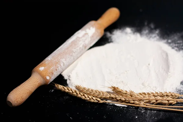 A kitchen rolling pin, spikelets of wheat, and a pile of white flour.