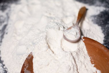 Bir fincanda beyaz buğday unu ve masa yüzeyinde. Tahta kaşık..