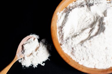 Kahverengi bardakta beyaz un. Tahta kaşık yakında. Masada bir avuç malzeme var..