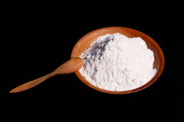 Bir fincan beyaz buğday unu ve masa yüzeyinde. Tabağın kenarında bir tahta kaşık duruyor..