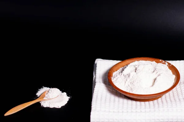 Cucchiaio di legno con farina di grano sparsa su una superficie scura. Una tazza con un mucchio di ingredienti su un tovagliolo bianco. — Foto Stock