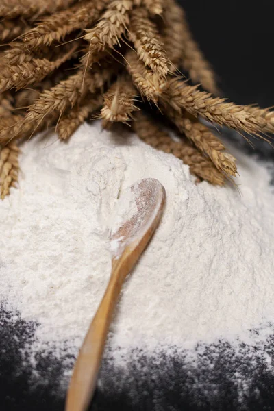 Un mucchio di spighe di grano nella parte superiore dello schermo. Un cucchiaio di legno è posto su una pila di farina bianca. — Foto Stock