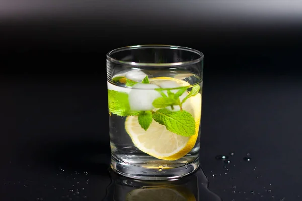In a glass of water, ice cubes, a sprig of mint and a slice of lemon. — Stock Photo, Image