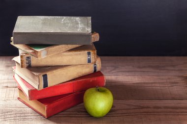 Eski kitaplar vintage ve rustik ahşap bir masa üzerinde bir yeşil elma yığını.