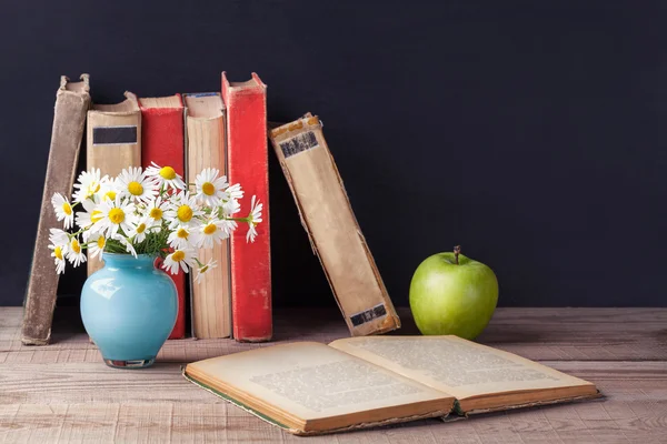 Abierto viejo libro vintage se encuentra en una mesa rústica de madera, en la que se encuentra un jarrón azul con margaritas y manzana verde. País bodegón . —  Fotos de Stock