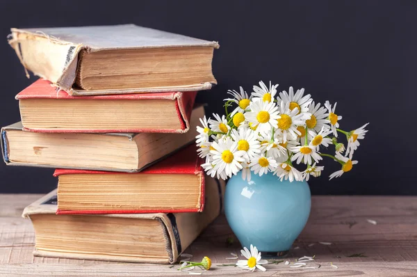 Ein Stapel alter Bücher liegt auf einem Holzregal mit einem Strauß Gänseblümchen in einer blauen Vase. Stillleben auf dem Land. — Stockfoto