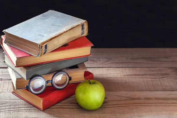 Una pila de libros antiguos y una manzana verde sobre una mesa de madera rústica . —  Fotos de Stock