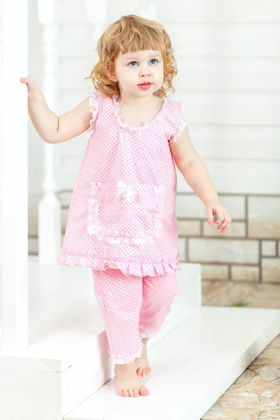 Little curly girl in a pink dress and bare feet coming out of the house and go down the stairs
