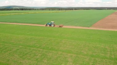 Sahada uçan İHA ve yer yolunda giden mavi tarım traktörü..